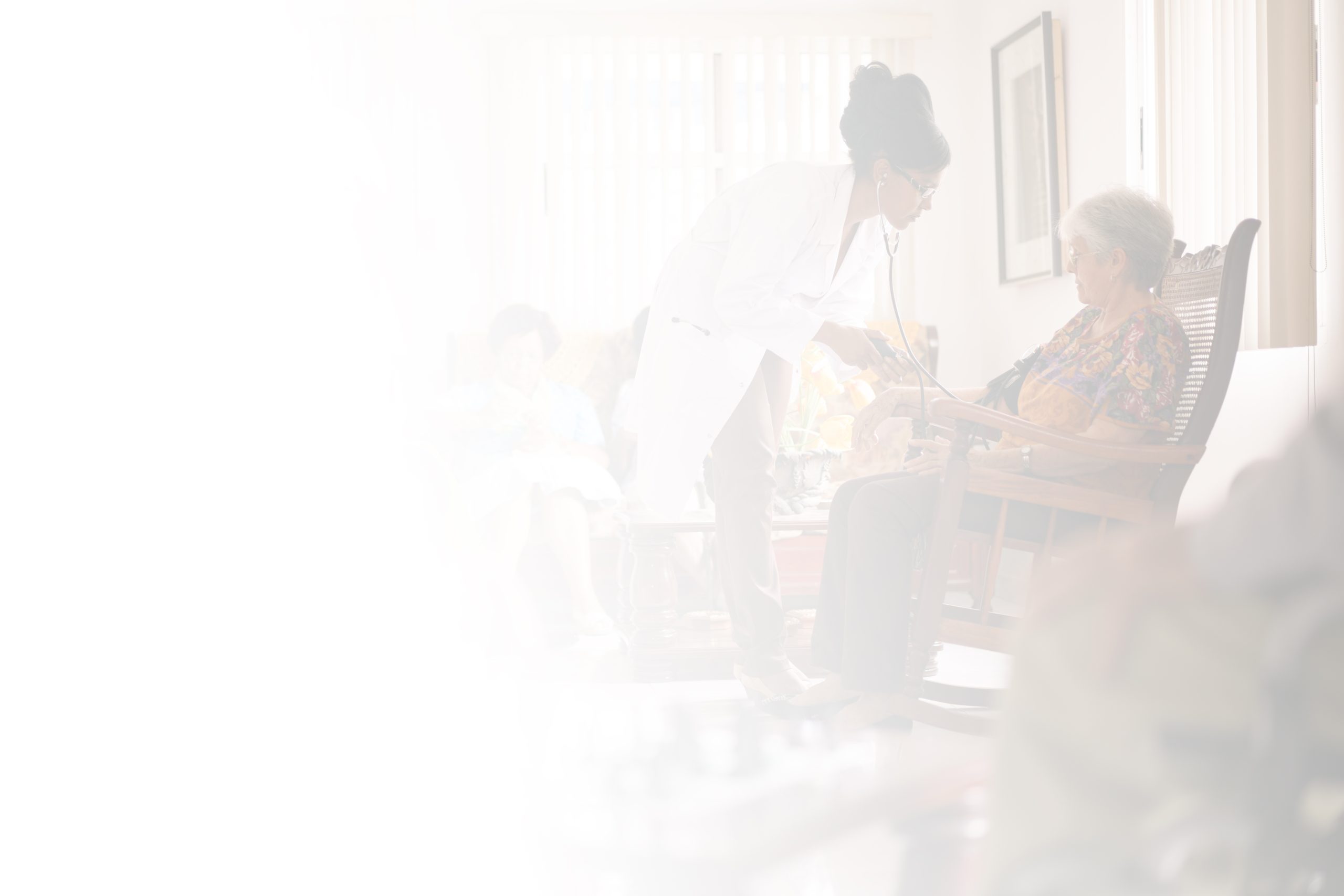 A doctor wearing a white coat listens to an elderly woman's heartbeat with a stethoscope in a well-lit room at North Pines Assisted Living. The elderly woman is seated in a chair, while other residents are seen in the background. The image has a faded, light effect on the left side.