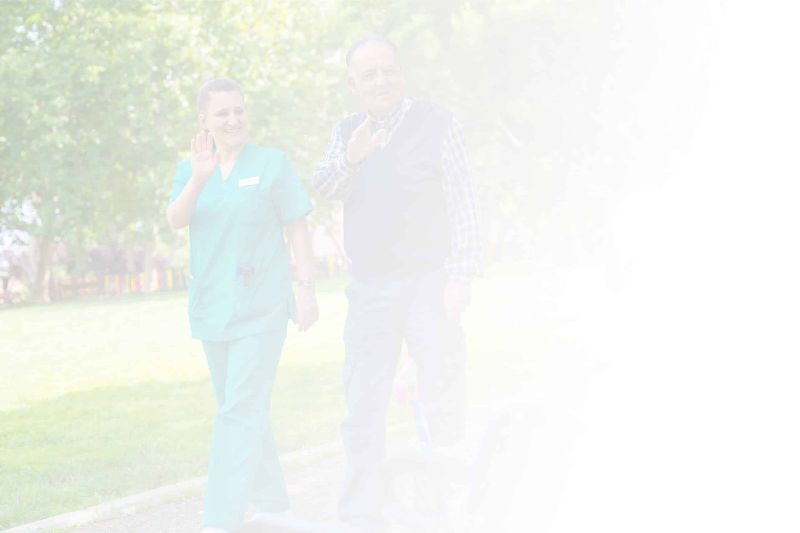 A smiling woman in green medical scrubs walks alongside an elderly man in a plaid shirt and dark vest. They are outdoors on a sunny day at North Pines Assisted Living, waving and acknowledging someone. The background features lush green trees and a sunlit park scene, epitomizing the serene environment of this senior living facility.