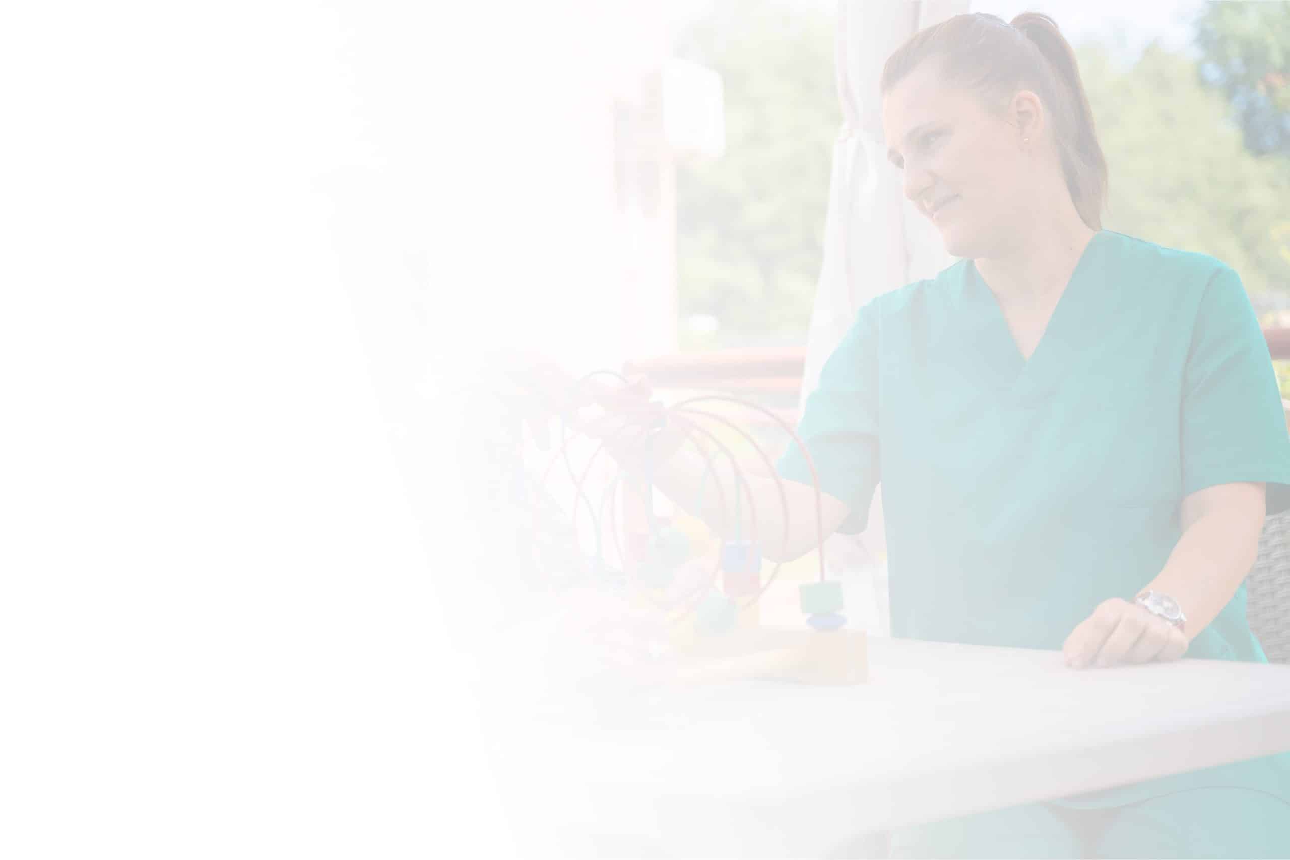 A woman in green scrubs sits at a table outdoors at North Pines Assisted Living, engaging with what appears to be a child (faintly visible) in a playful activity involving a bead maze. She smiles, creating a warm and caring atmosphere. The image has a soft, ethereal quality with a bright, hazy filter.