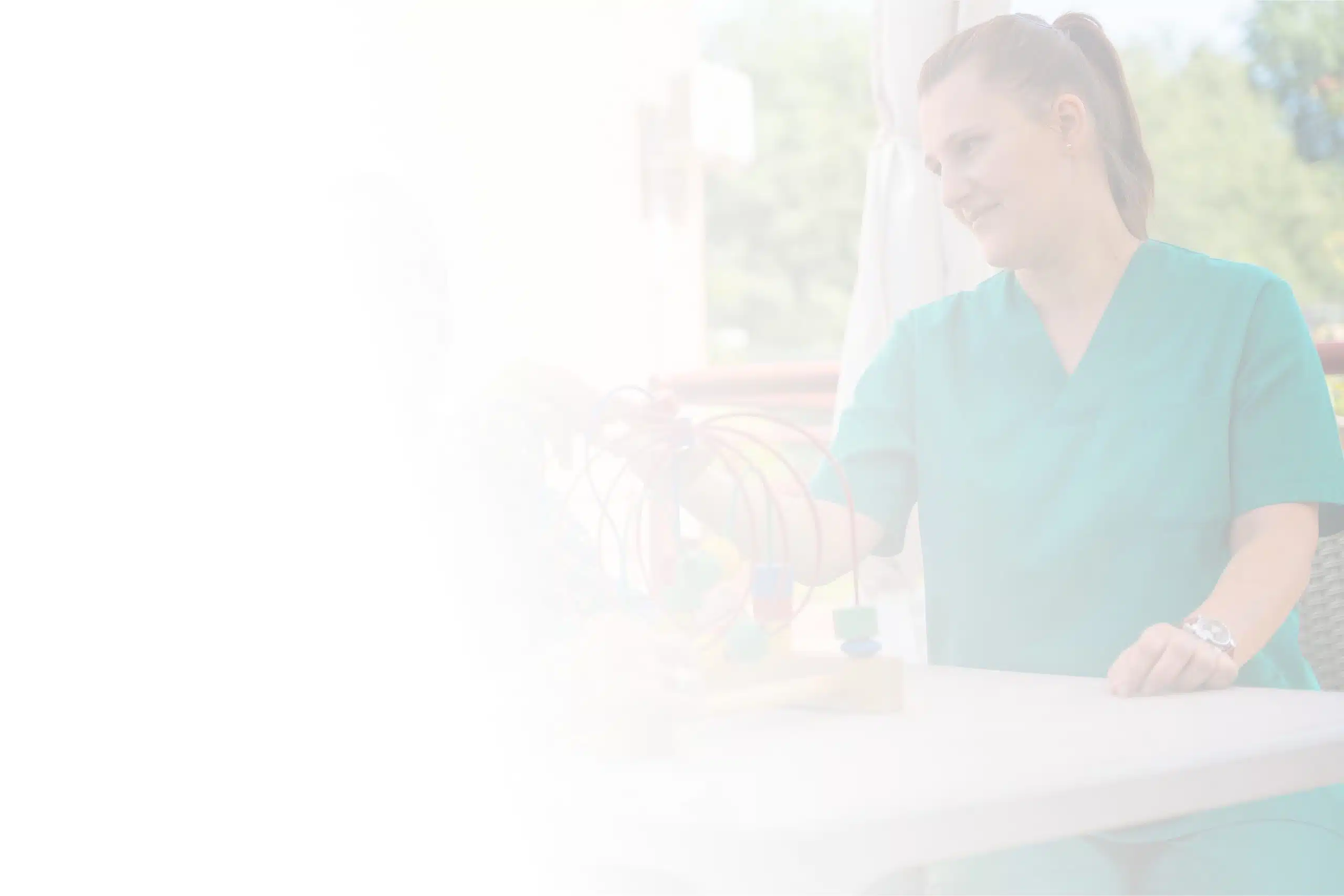 A woman in green scrubs sits at a table outdoors at North Pines Assisted Living, engaging with what appears to be a child (faintly visible) in a playful activity involving a bead maze. She smiles, creating a warm and caring atmosphere. The image has a soft, ethereal quality with a bright, hazy filter.