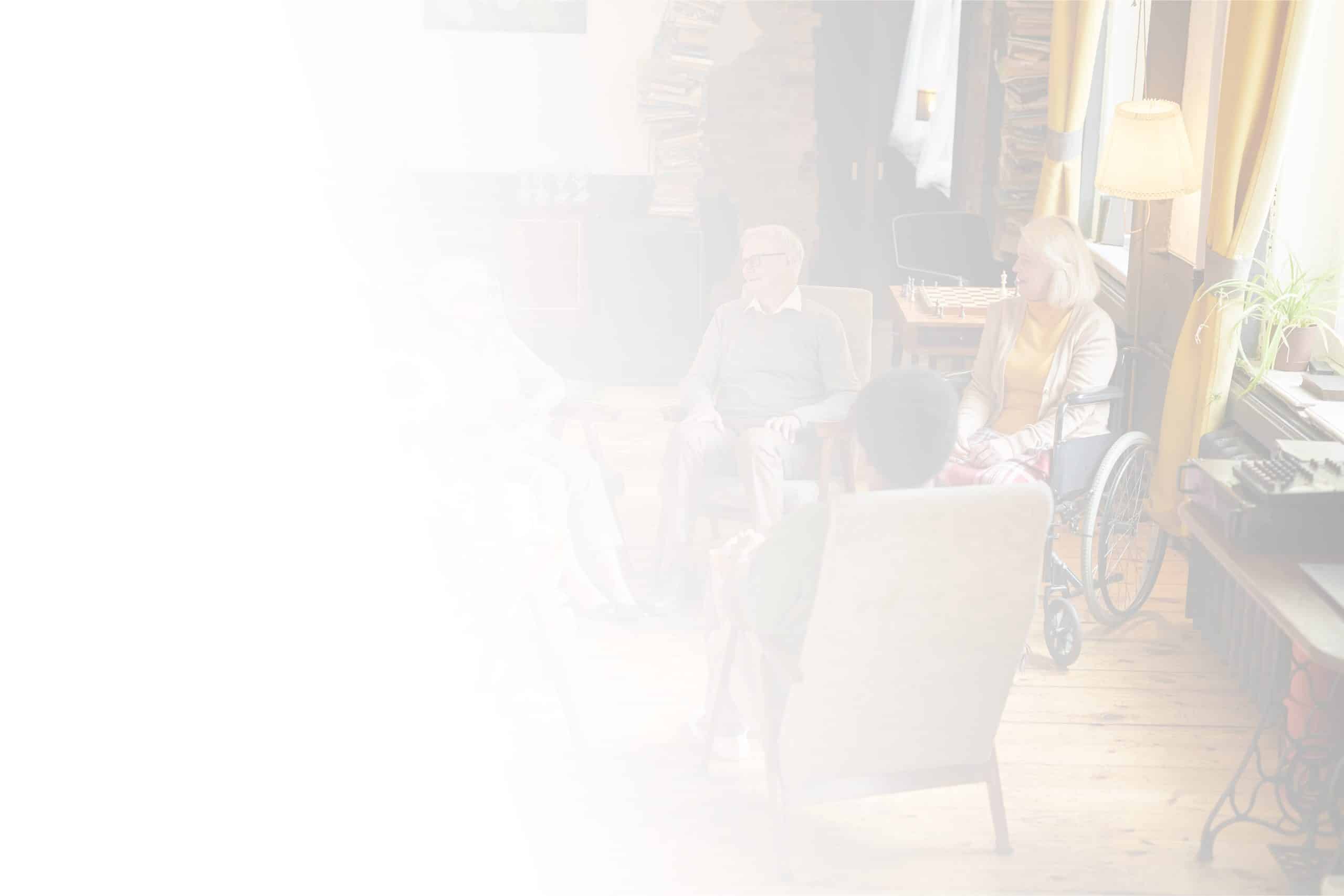 A group of elderly people are sitting in a well-lit room with wooden floors at North Pines Assisted Living. One person is in a wheelchair, and another sits in a recliner. The room has a cozy ambiance with warm lighting and shelves filled with books in the background, embodying the comfort of an excellent senior living facility.