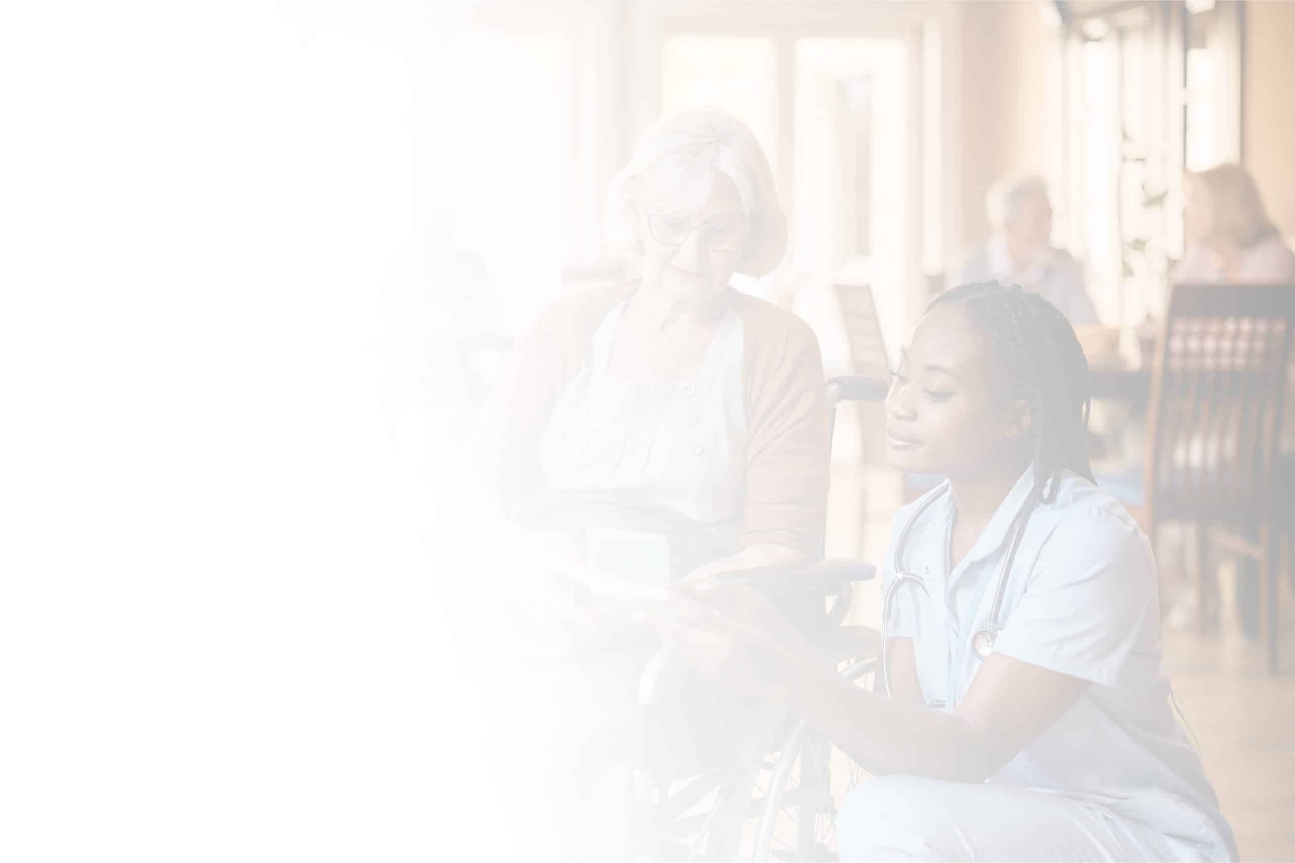 A nurse in scrubs kneels beside an elderly woman in a wheelchair at North Pines Assisted Living, showing her something on a piece of paper. The background reveals a bright, softly blurred room with other people. The image features a light gradient on the left, transitioning to clear on the right.